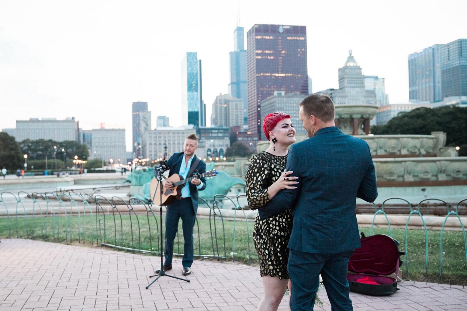A newly engaged couple embraces at Buckingham Fountain while JD Kostyk performs