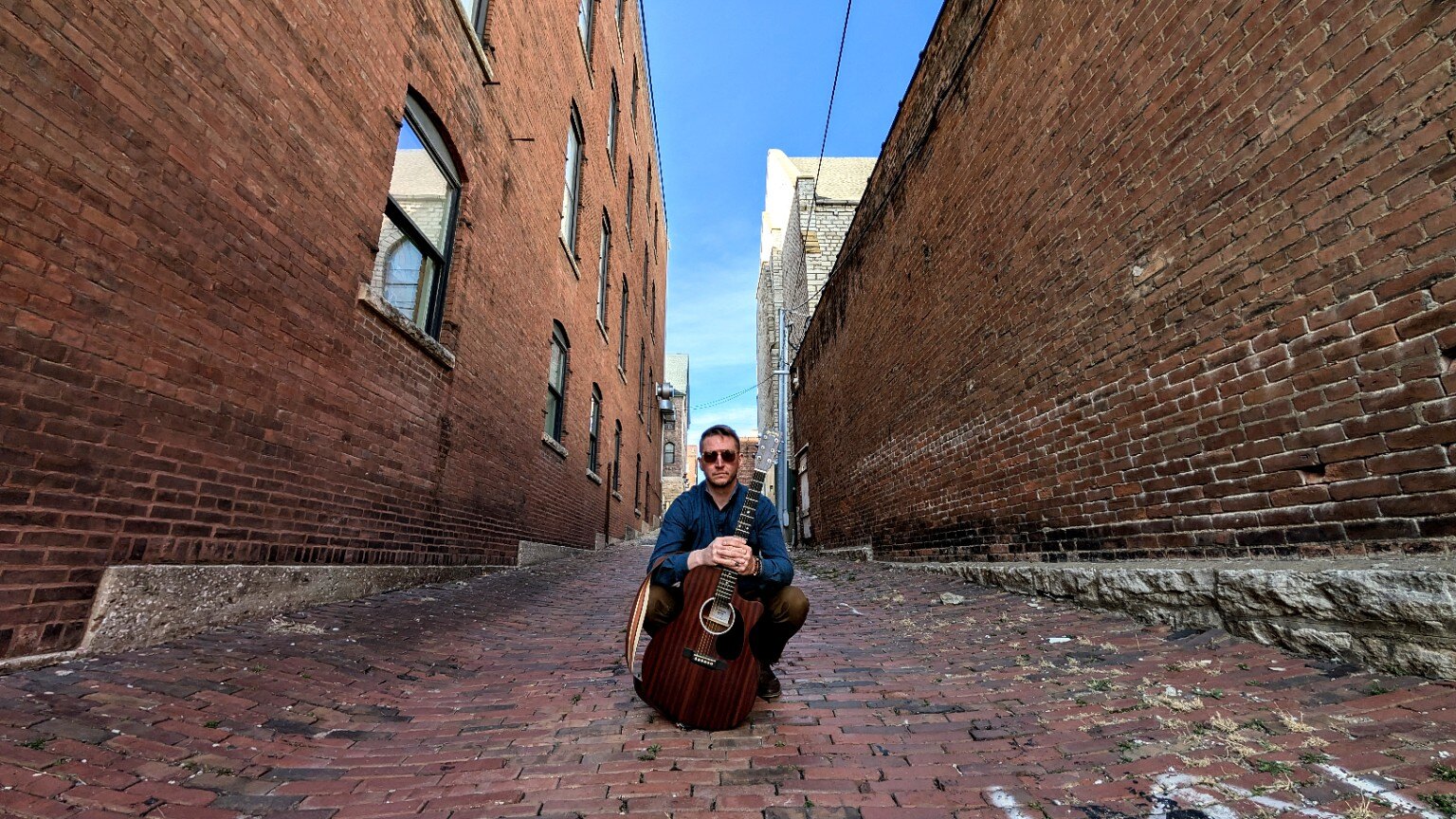 JD Kostyk with an acoustic guitar in a Chicago alley